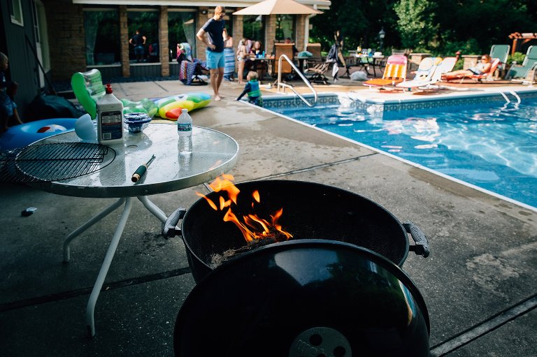 Lit grill with backayrd pool out of focus. 