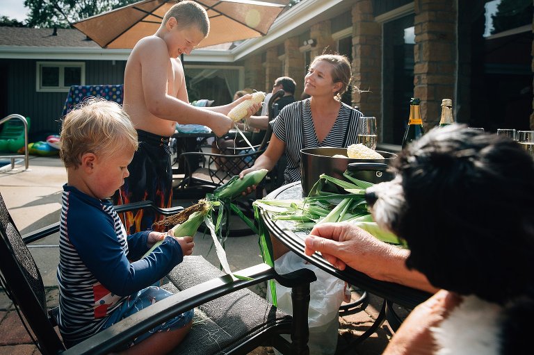 three people shuck corn outside in the sun. 
