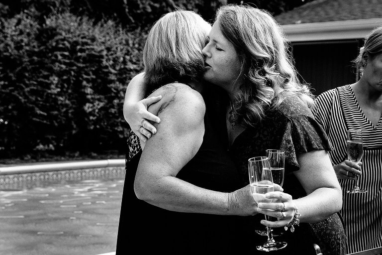 Black and white. Two women emotionally hug while holding champagne glasses. 