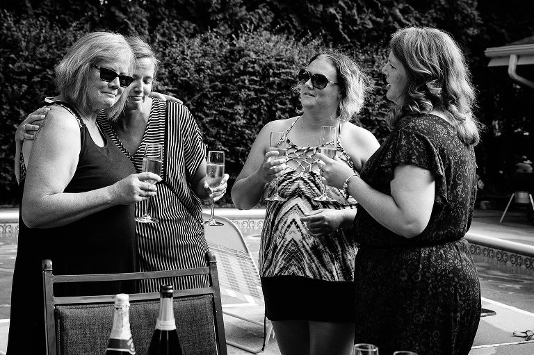 Black and white. Four women hold champagne glasses and hug. 