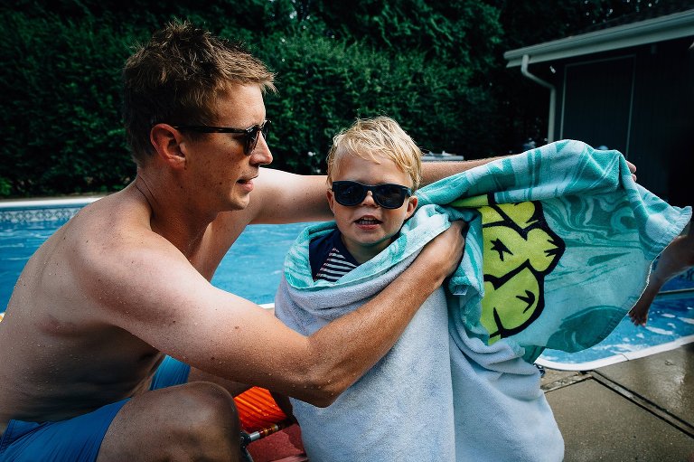 Boy gets wrapped in a towel coming out of the pool. 