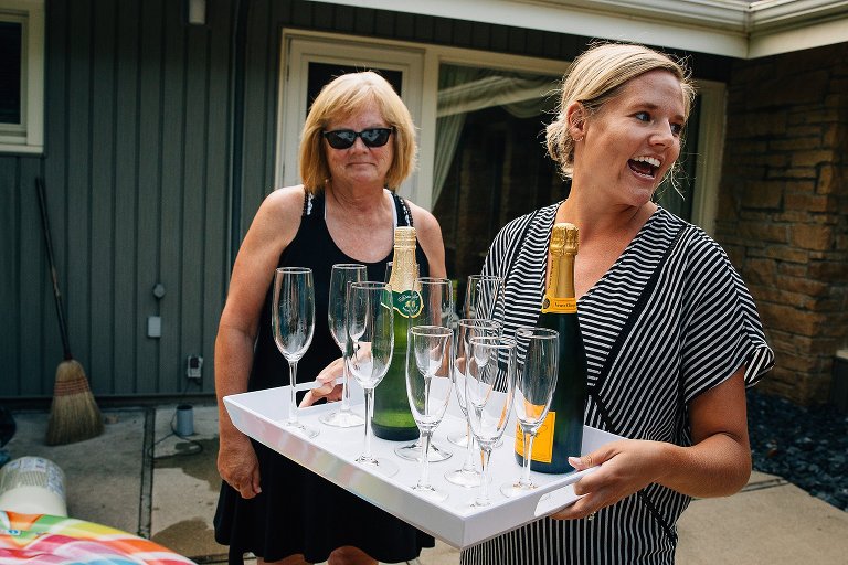 two women bring a tray of champagne and apple juice and glasses outside 