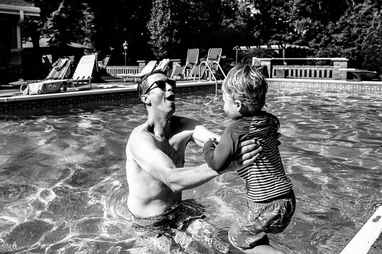 black and white. Boy jumps into water, Dad joyfully catches him. 