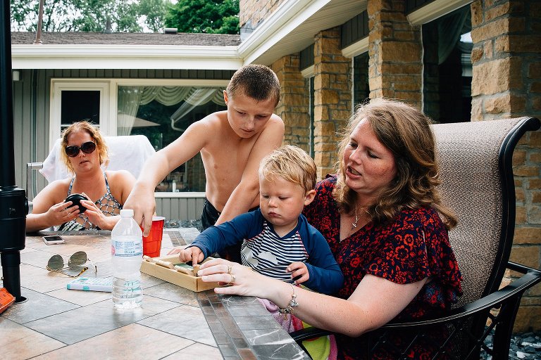 Two women play a game with two young boys at a picnic table outside. 