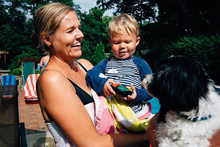 Mom holds young son while wrapped in beach towels. Both are smiling. Small black dog in the foreground. 