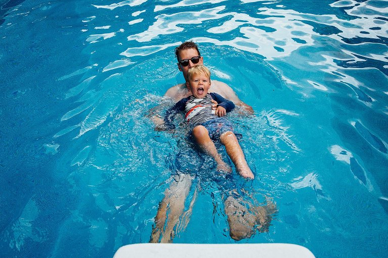 Dad holds young son on his belly while they float on dad's back across the pool. 