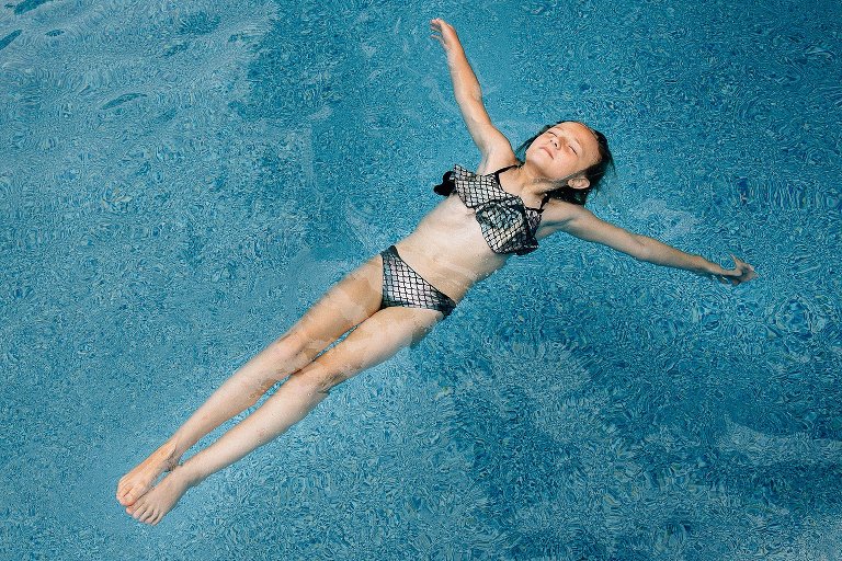 Girl floats on her back in the pool with arms stretched out. 