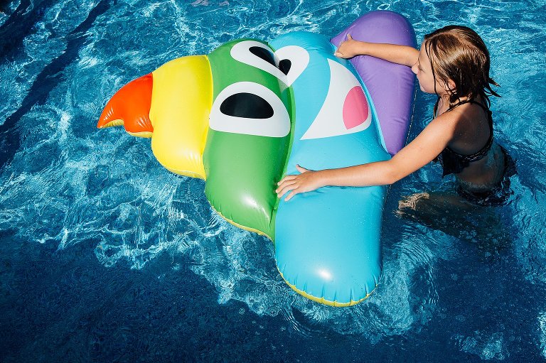 Young girl holds a rainbow poop emoji flotation device in the pool. 