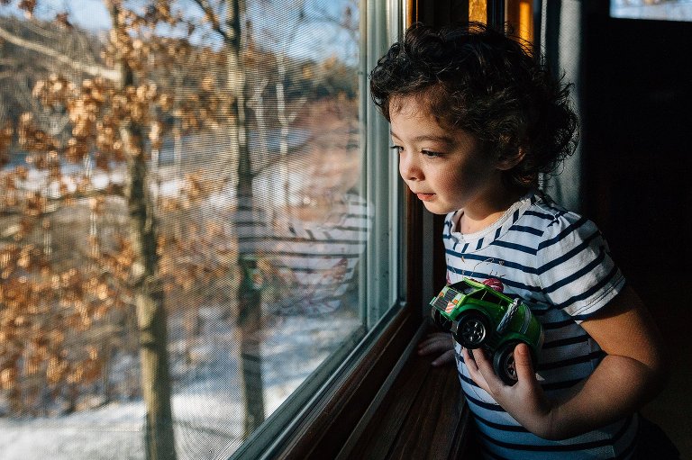 Girl holds a green truck while looking out window on a snowy day