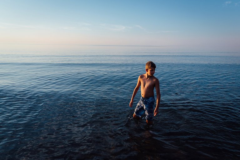 teen boys stands in shallow water at sunset 