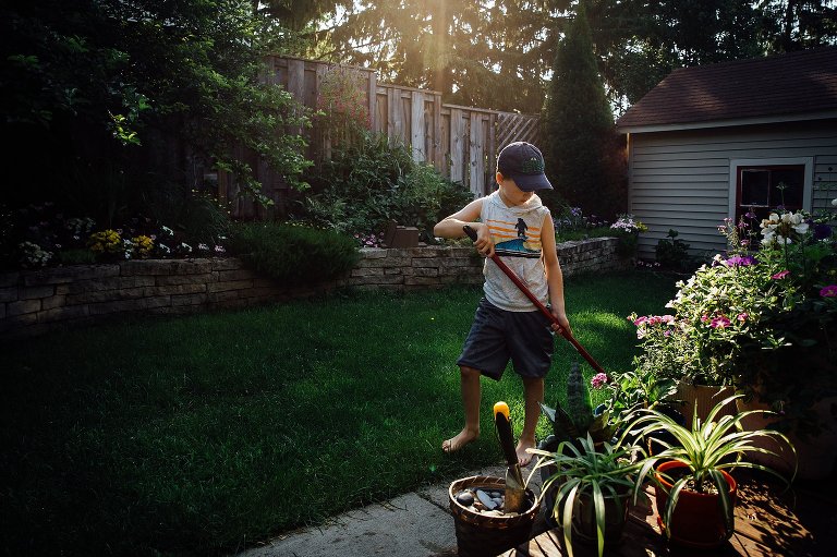 boy sweeps small backyard on summer morning