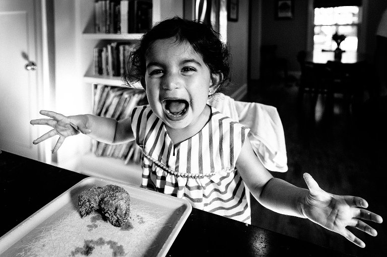 Black and white. Girl is super smiley while eating a freshly baked homemade apple cider donut