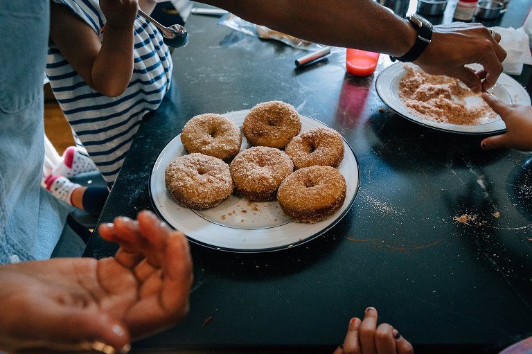 Prepared apple cider donuts on the table while hands working to make more in the background 