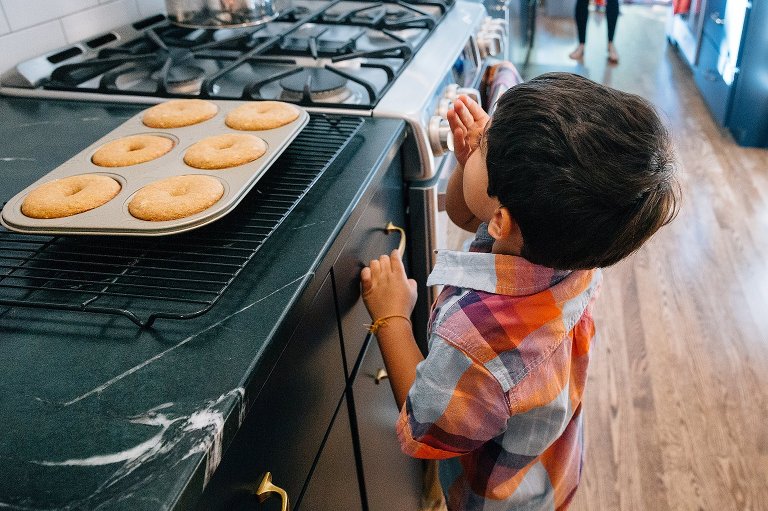 Boy stands next to kitchen counter with freshly baked donuts using his hand to waft the smell toward him 