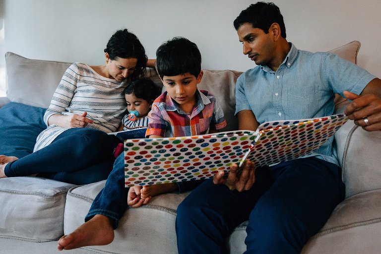 Family of 4 reads two different books on the couch together during a Madison family photographer session