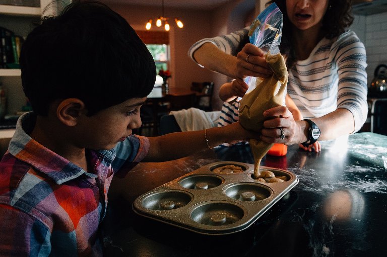 Mom holds bag of donut dough while son guides it into the prepared pan during a Madison family photographer session