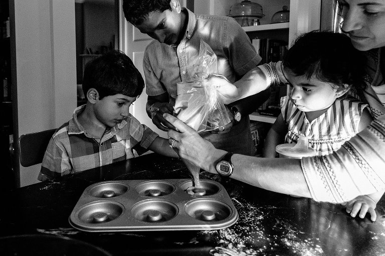 black and white. Tight crop of family of 4 squeezing donut dough into prepared pans during a Madison family photographer session