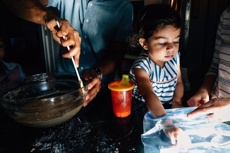 dad stirs, daughter reaches in bag while baking in the kitchen during a Madison family photographer session