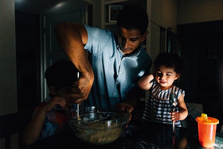 Dad stirs the ingredients in dramatic light with toddler smiling during a Madison family photographer session