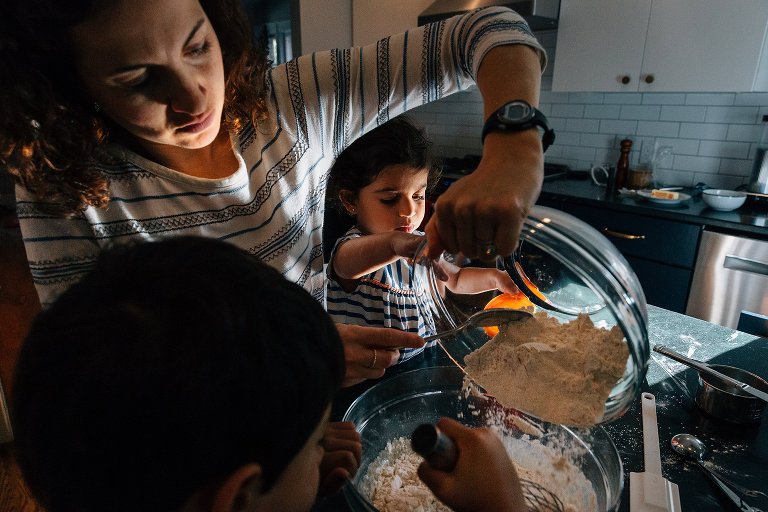 Mom helps move dry ingredients to a second bowl while two kids help make donuts during a Madison family photographer session