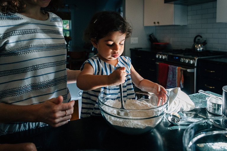 Toddler girl stirs the flour in a bowl during a Madison family photographer session