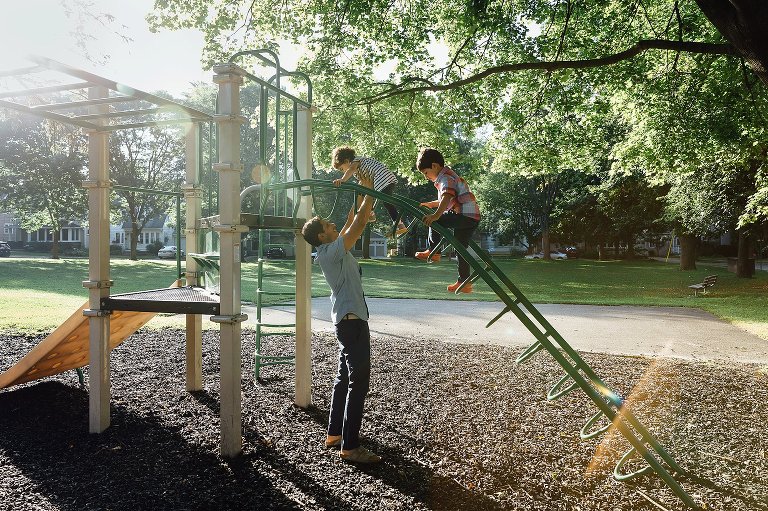 Dad reaches arms to daughter climbing playground equipment while son follows during a Madison family photography session