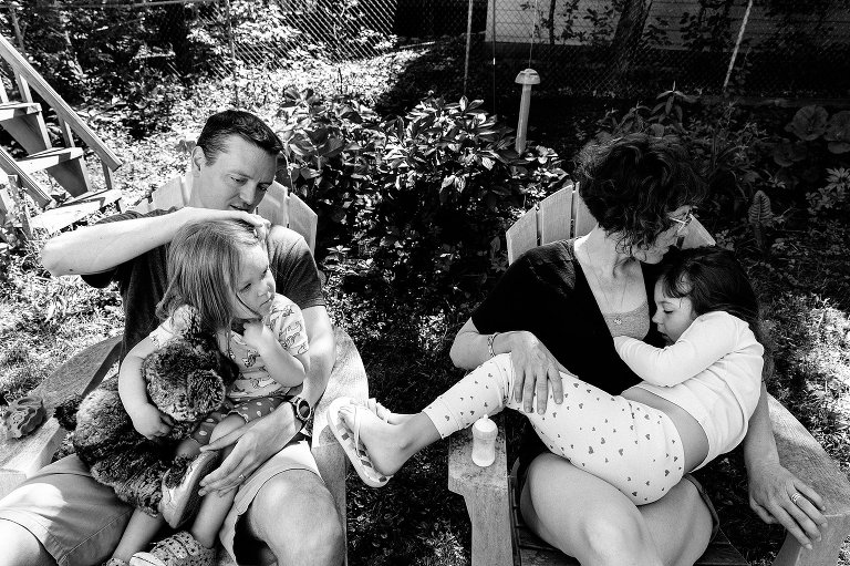 Black and white. mom and dad and two daughters sit on chairs and connect in the backyard on a spring Saturday morning 