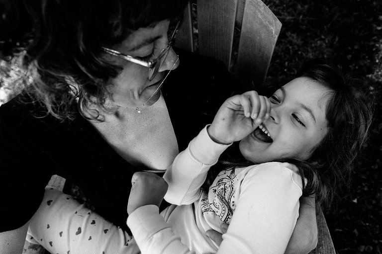 Black and white. mom and daughter laugh in a chair together 