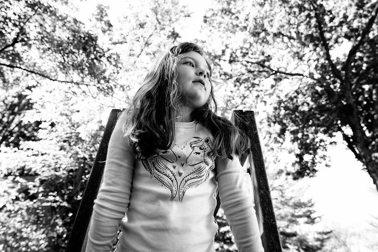 black and white. Girl is on swing set looks up, head in spring trees 