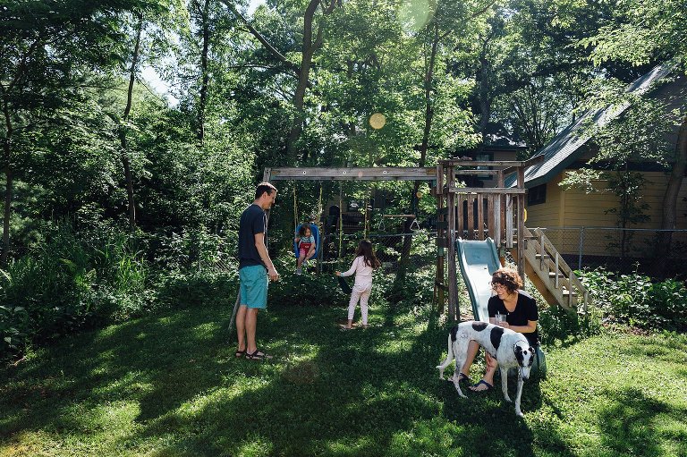 Family of four play on swing set in backyard on a spring Saturday morning 