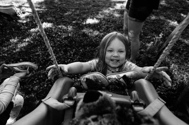 black and white. Girl reaches into swing pushing stuffed animals, smiling