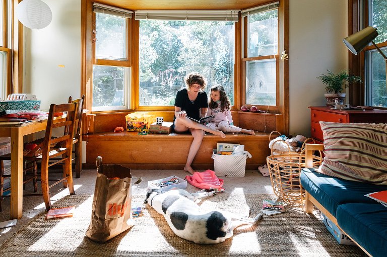 Mom and daughter read in on the window bench while dog sleeps in the sun