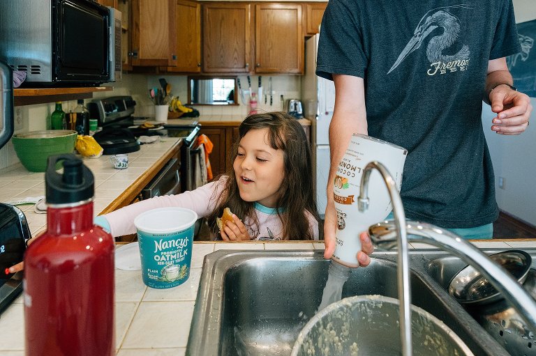 girl pushes blender button and smiles while dad pours out rinsed almond milk 
