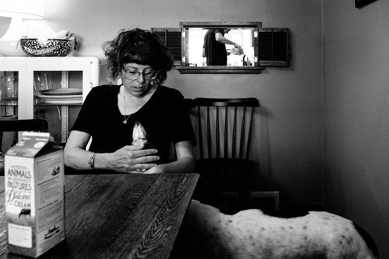 woman holds dog's face while man pours a bottle in the background 