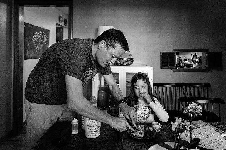 Black and white. Dad cuts daughter's pancakes at dining room table