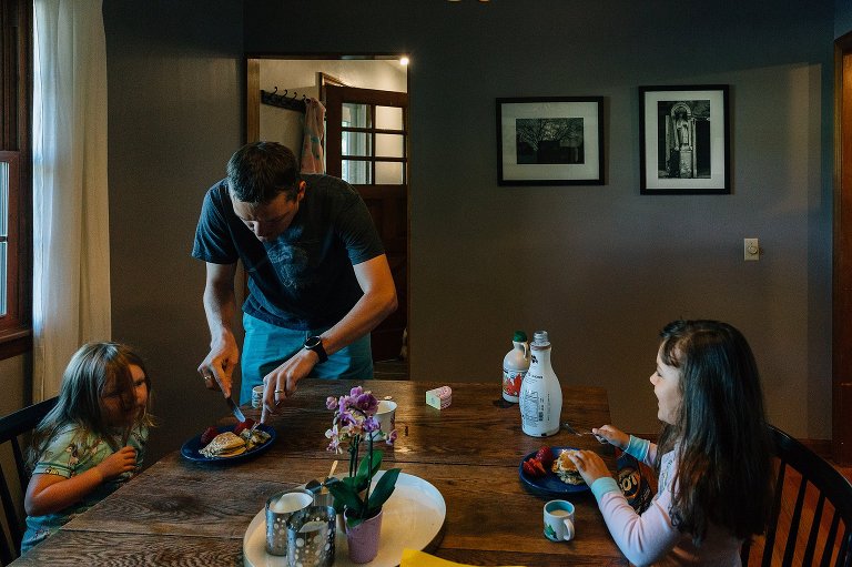 Dad cuts pancakes in the dining room with two daughters