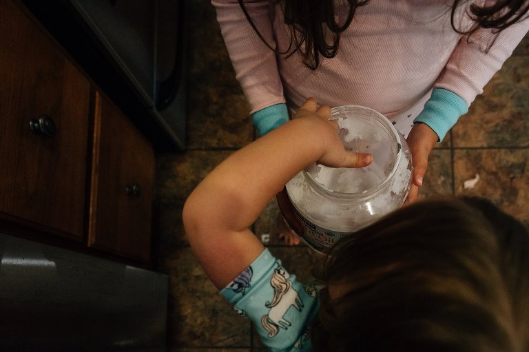 Two girls reach into coconut oil container 