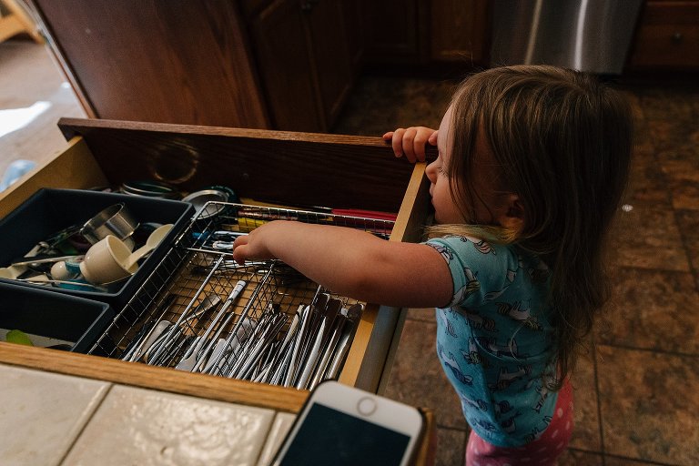 young girl reaches into silverware drawer for utensils 