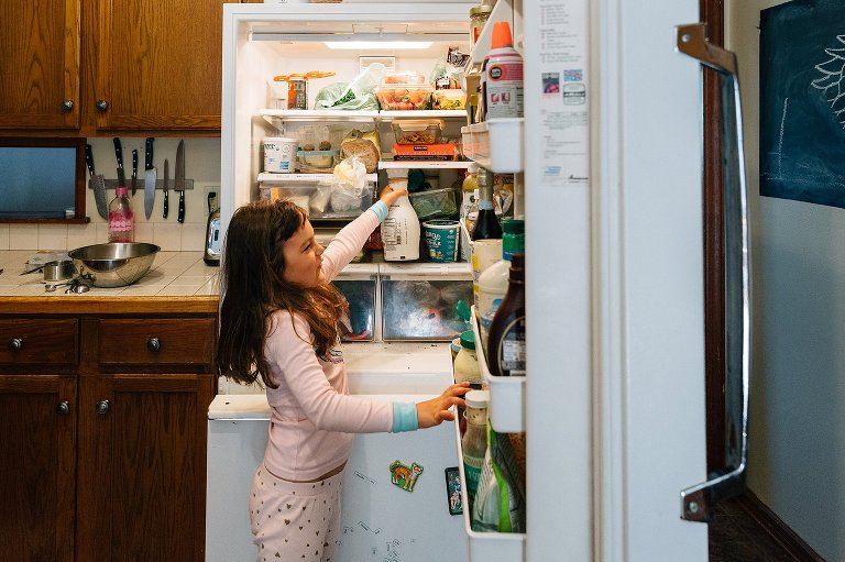 girl reaches for almond milk in refrigerator 