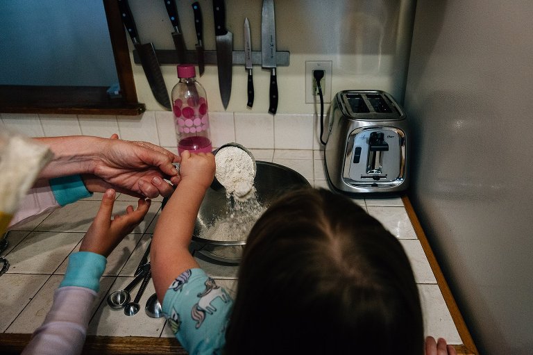 Many hands pouring flour into a big steel bowl