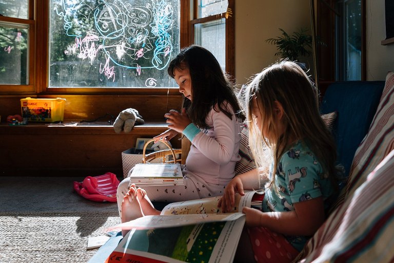Two young girls sit on couch and read books on Saturday morning 