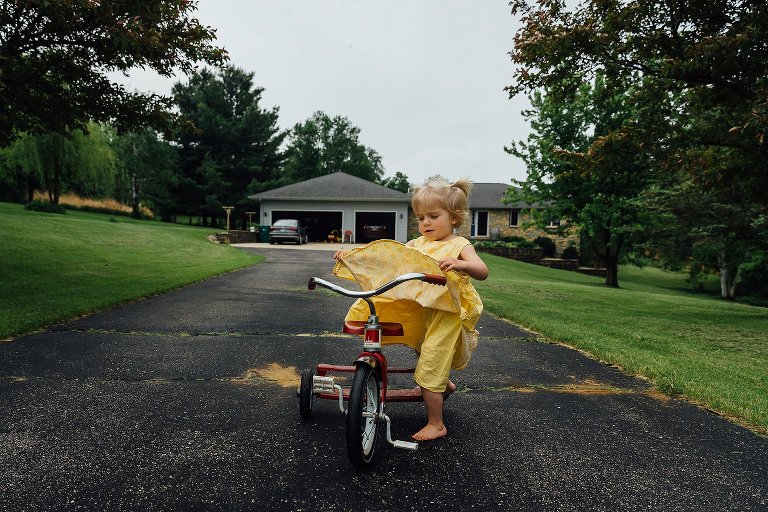 Young girl pulls up her yellow dress while getting on red trike