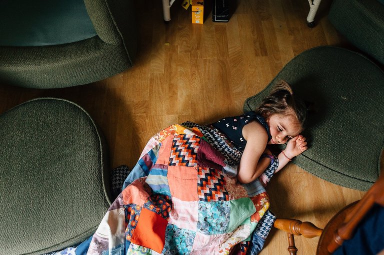 young girl rests on makeshift nest of pillows and quilt on the floor