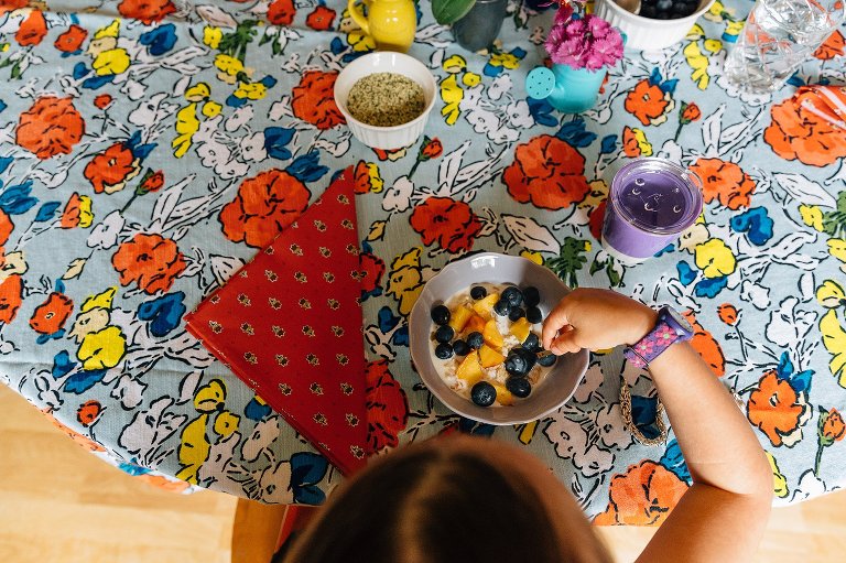 Top down view. Young girl puts berries in her oatmeal on colorful table.