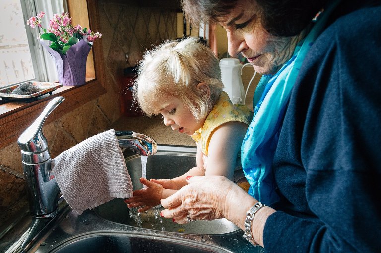 Grandmother helps granddaughter wash her hands in the kitchen sink