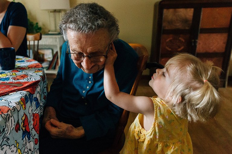 Toddler in yellow dress touches her great-grandmother's hearing aid 