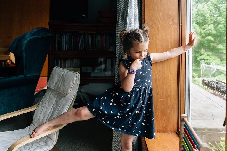 Young girl holds onto window and stretches out leg. 