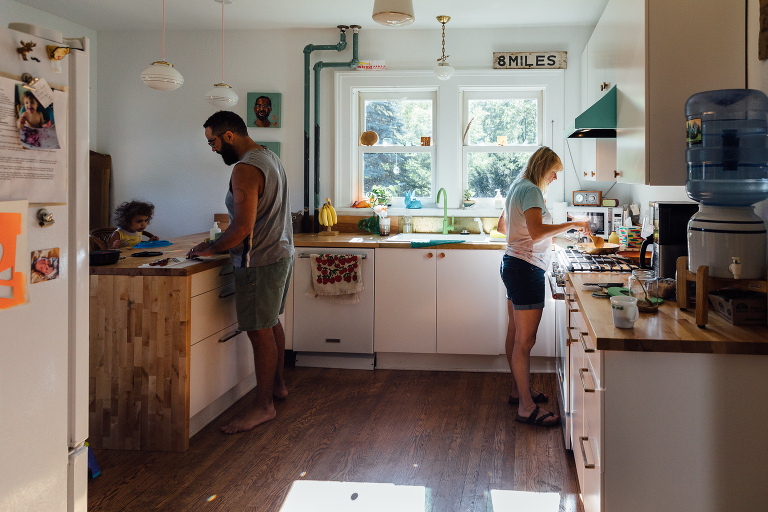 Two parents and young girl make breakfast in a light-filled kitchen on a summer's day. Family documentary. 