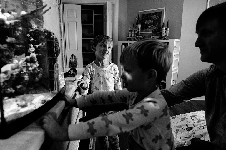 layered image. Man holds son in his lap while son looks at fish tank while another son talks and smiles at dad 