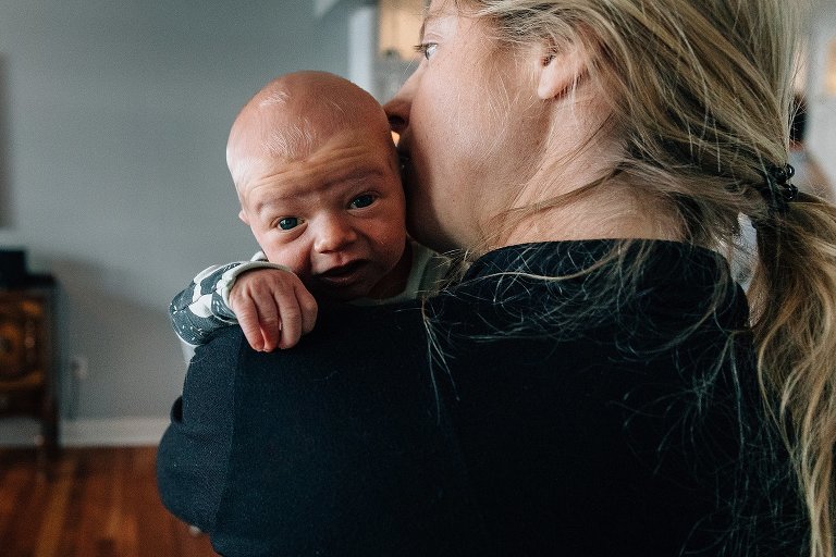 newborn at home is propped over mom's shoulder, awake & making eye contact with camera 